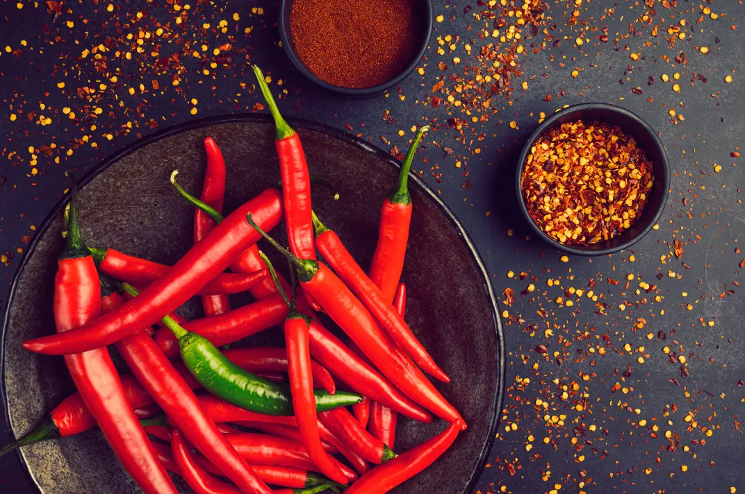 Photo de piments rouges sur fond gris, parsemé d'épices