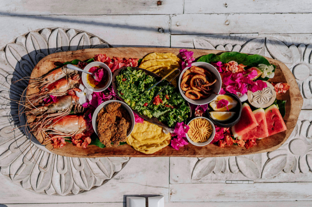 Photo d'un plateau de fruits de mer sur un support en bois. Il y a des crevettes, de la pastèque et de la tartinade.