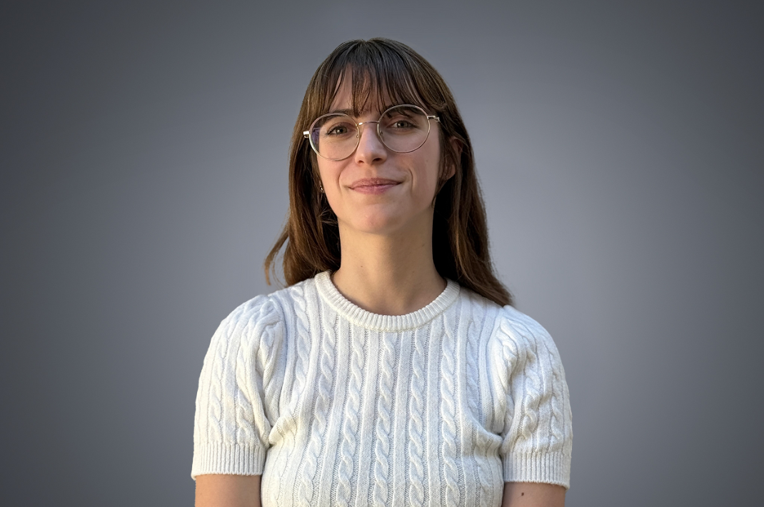 Julia, Assistante Supply Chain. Elle se tient droite derrière un fond gris.